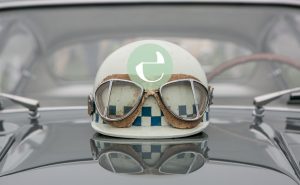 hvid racerhjelm med retro racer briller ovenpå motorhjelmen af ældre bil med essencius logo i forgrunden